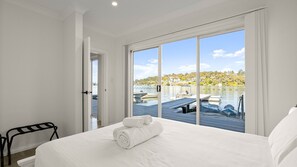 A hotel room with a large bed, a view of boats on a lake, and a door leading to a balcony. - The Oatley River House with Jetty & Water Views (Oatley)