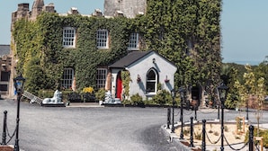 A castle-like building with a prominent tower, ivy-covered walls, and a small adjacent structure with a red door. - Cloonacauneen Castle (Galway)