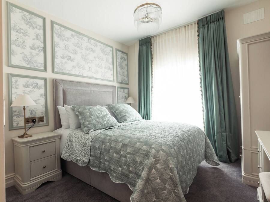 A bedroom with a bed, nightstands, a lamp, a dresser, and a window with curtains.