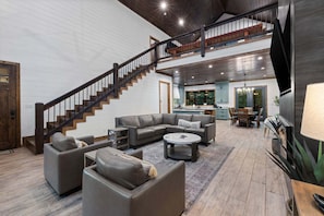 Un amplio salón con una escalera, un conjunto de sofás, una mesa de centro y una cocina al fondo.
