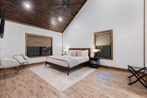 Une chambre avec un plafond en bois, un grand lit, deux tables de chevet, une fenêtre donnant sur un beau paysage et un fauteuil.