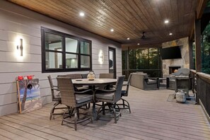 An outdoor patio with a round table and chairs, a stone fireplace, and a TV mounted on the wall. - 5BR Hochatown Cabin: Hot Tub - Game Room - Fits 13 - Min to Lake & Casino (Broken Bow)