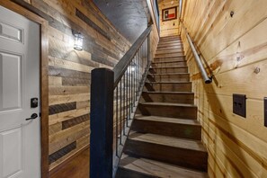 A wooden staircase with a metal handrail and a white door on the left. - Hochatown Luxury Cabin on 1+ Acre: Main Lodge + Detached Private Suite & Stream (Broken Bow)