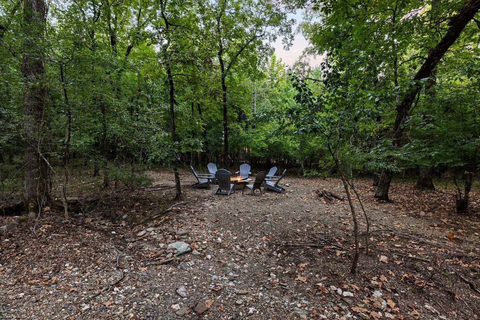 Un espace extérieur aménagé avec des chaises Adirondack et une table, entouré d’une forêt dense.