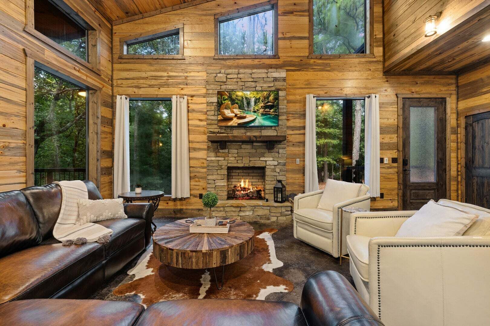 A log cabin interior with a stone fireplace, leather sofas, and a cowhide rug.
