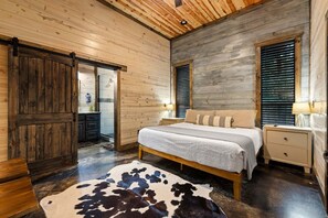 Un dormitorio con techo de madera, una cama con colcha blanca, una mesita de noche, un aparador y un tapiz de cuero de vaca.
