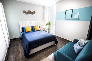 Ein Schlafzimmer mit einem Bett, einer Couch, einer Zimmerpflanze und einer Wand mit dekorativen Tellern.