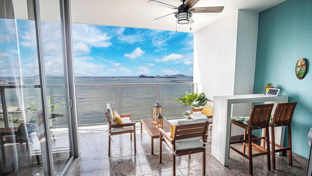 Un balcone con vista sul mare, una ventola a soffitto e un tavolo con sedie.