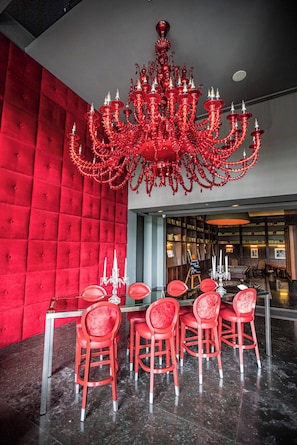Eine rote Wand mit Polsterung, ein roter Kronleuchter und rote Stühle um einen Tisch in einem Raum.
