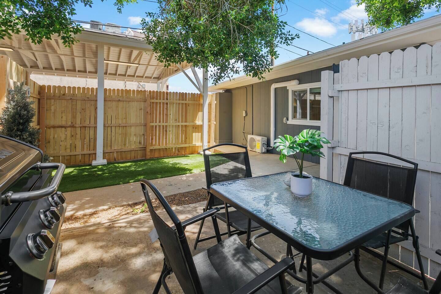 An outdoor patio with a grill, a table with chairs, and a potted plant.