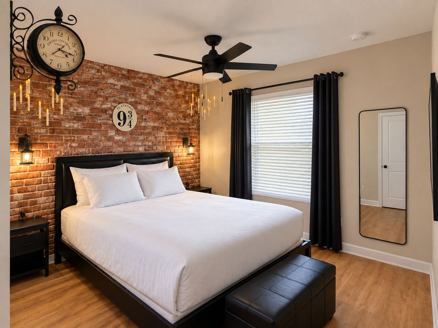 Une chambre avec un mur en briques, un lit, un ventilateur de plafond, une horloge et une fenêtre avec des rideaux.