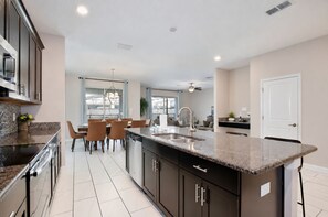 A modern kitchen with a central island, built-in appliances, and a dining area with chairs. - Walk to Lazy River - Themed 6BR Home - Private Pool, Spa and Game Room, Store... (Kissimmee)