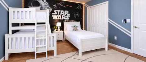 Een slaapkamer met een Star Wars thema aan de muur, een stapelbed, een enkel bed, een nachtkastje en een deur.