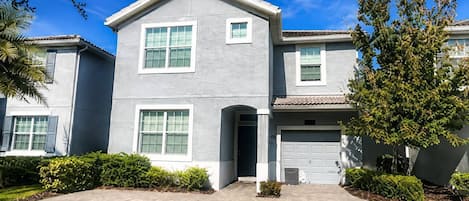 Un immeuble résidentiel à deux étages, doté d’une façade grise, d’un garage à l’avant et d’une allée bien entretenue.