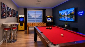 Una habitación con mesa de billar, mesa de fútbol de mesa y dos máquinas de arcade.