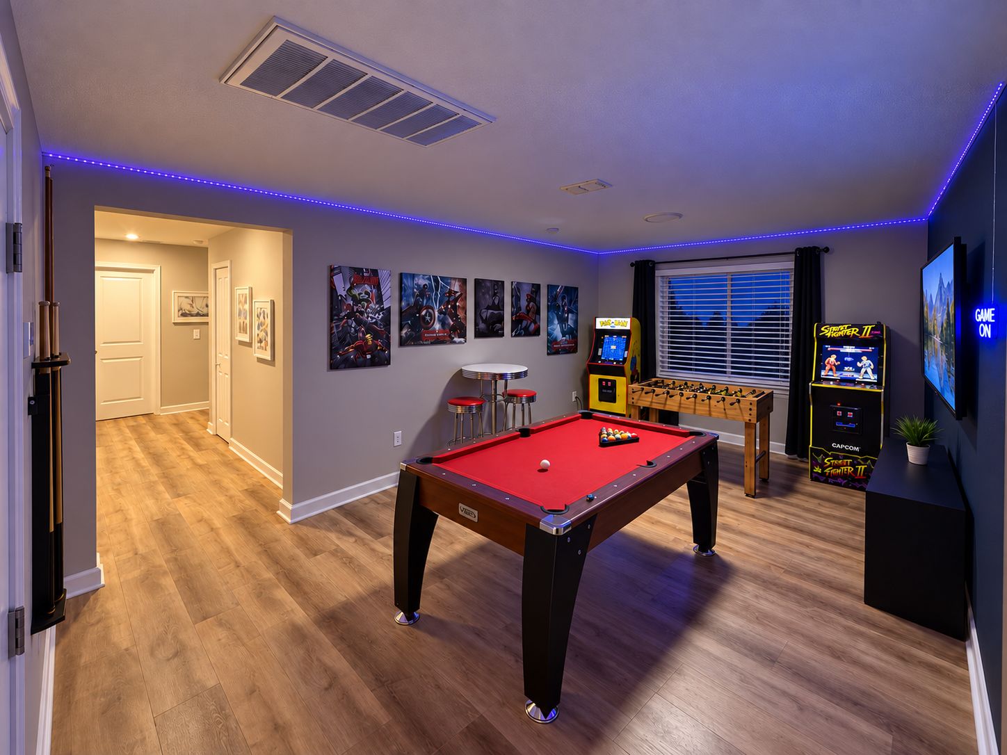 A pool table in a room with a foosball table, arcade games, and a TV screen displaying 'GAME ON'.