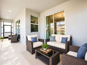 A modern outdoor seating area with wicker furniture and a glass coffee table. - Walk to Lazy River - Themed 6BR Home - Private Pool, Spa and Game Room, Store... (Kissimmee)