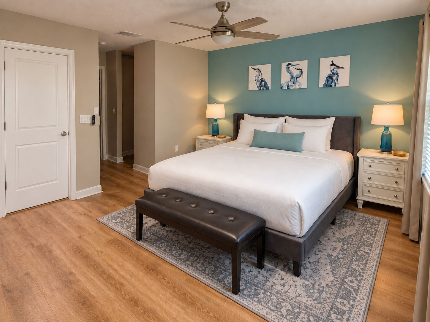 A bedroom with a bed, two bedside tables, a bench, a ceiling fan, and wall art.