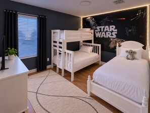 Un dormitorio con literas, una pared temática de Star Wars, una mesita de noche con una planta y una ventana con cortinas.