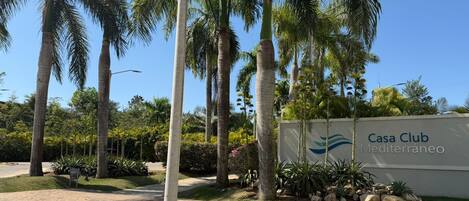 Une enseigne pour le Casa Club Mediterráneo, avec un jardin aménagé comprenant des palmiers et diverses plantes.