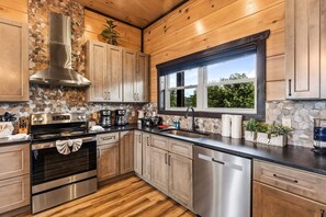 Eine moderne Küche mit Holzschränken, einer Stein-Spritzschutzwand, Edelstahlgeräten und einem Fenster mit Blick auf Grünflächen.