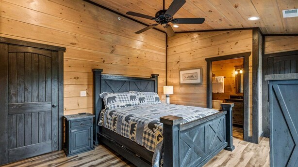 Een slaapkamer met houten lambrisering, een bed, een plafondventilator en een nachtkastje.