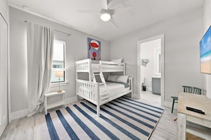 A child's bedroom with bunk beds, a ceiling fan, a window with curtains, a painting, and a beach scene on the wall. - New! Coral Tides + Brand 5BR New Luxury Build + Heated Pool + 1 Mile to Vanderbilt Beach! (Naples)