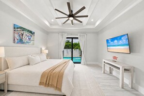 Une chambre avec un lit, un ventilateur de plafond, une télévision et une vue sur une piscine.