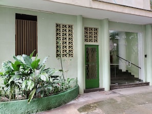 A building with a green door, a window with a decorative grille, and a staircase with a handrail. - Apartment on Copacabana Beach (Rio de Janeiro)