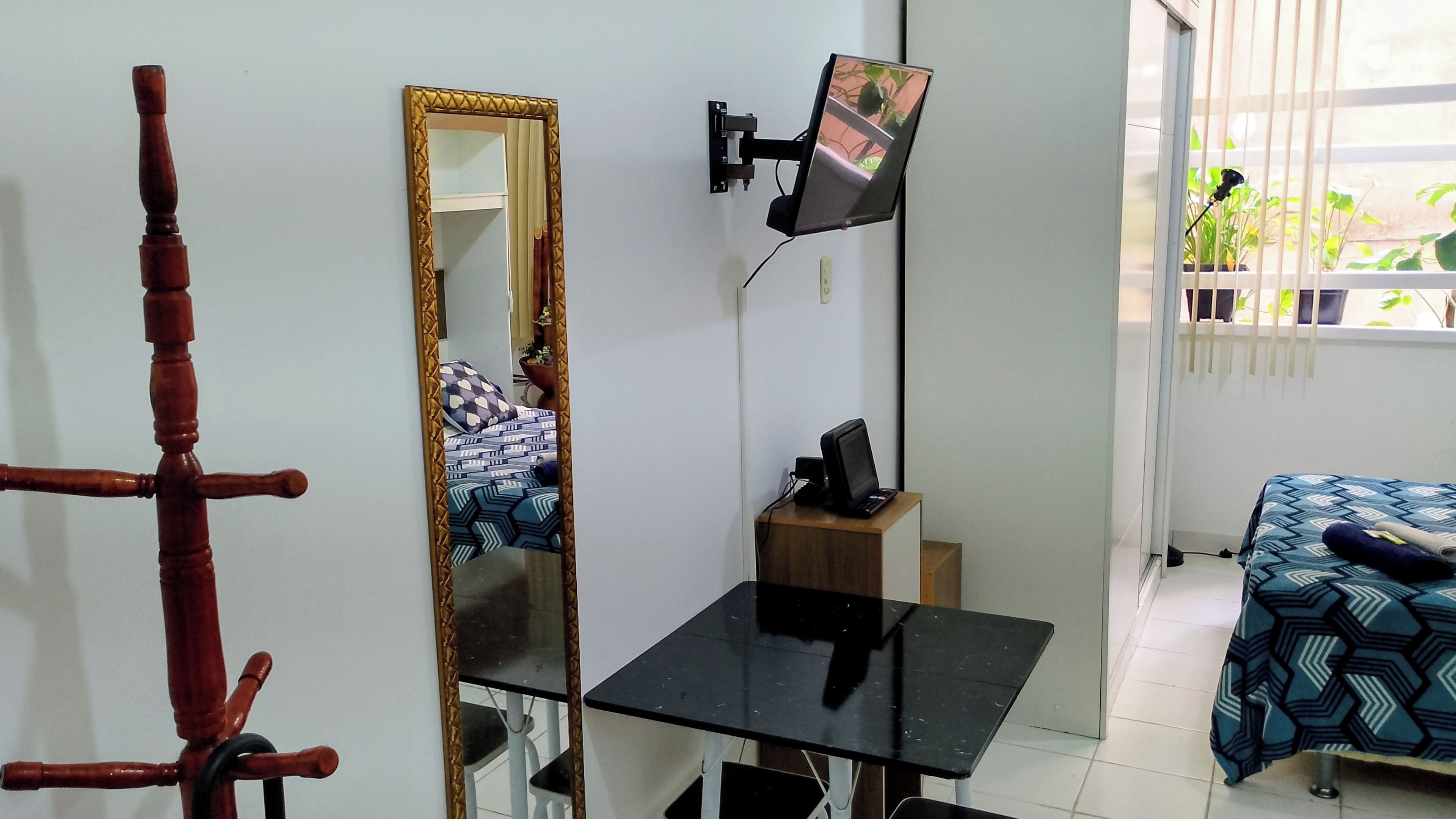 A room with a bed, a desk, a chair, a mirror, and a television mounted on the wall.