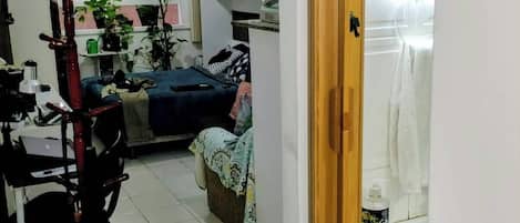 Una habitación con cama, escritorio y silla, una mesita y una ventana con plantas.