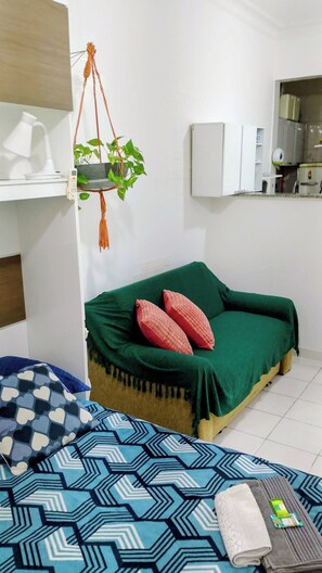 A small, cozy room with a bed, a hanging plant, a desk with a lamp, and a kitchenette area. - Apartment on Copacabana Beach (Rio de Janeiro)
