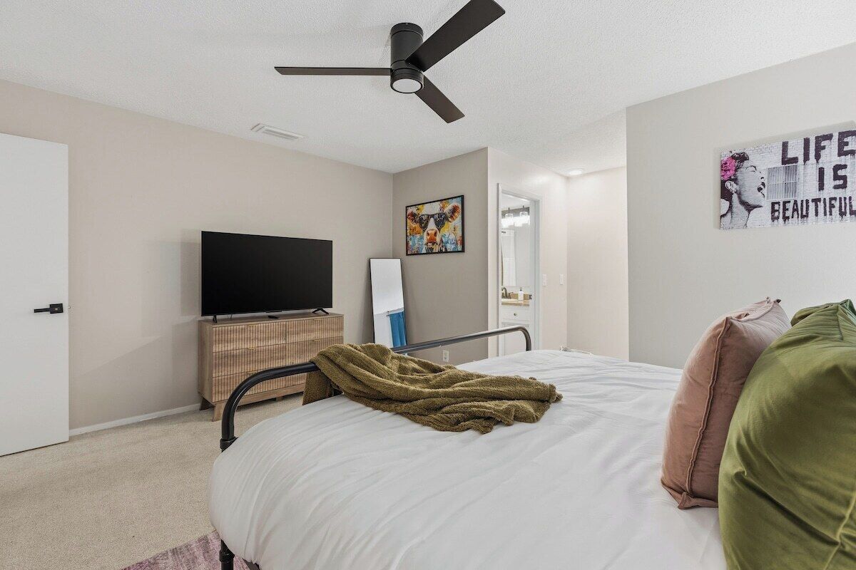 Un dormitorio con cama, televisión, ventilador de techo y una pared con un cartel.