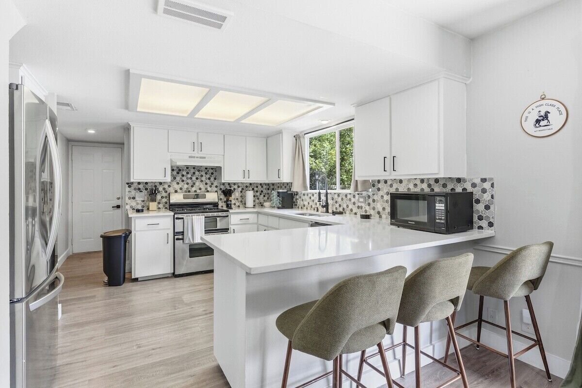 A modern kitchen with white cabinetry, a central island with bar stools, and a microwave.