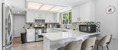 A modern kitchen with white cabinetry, a central island with bar stools, and a microwave.