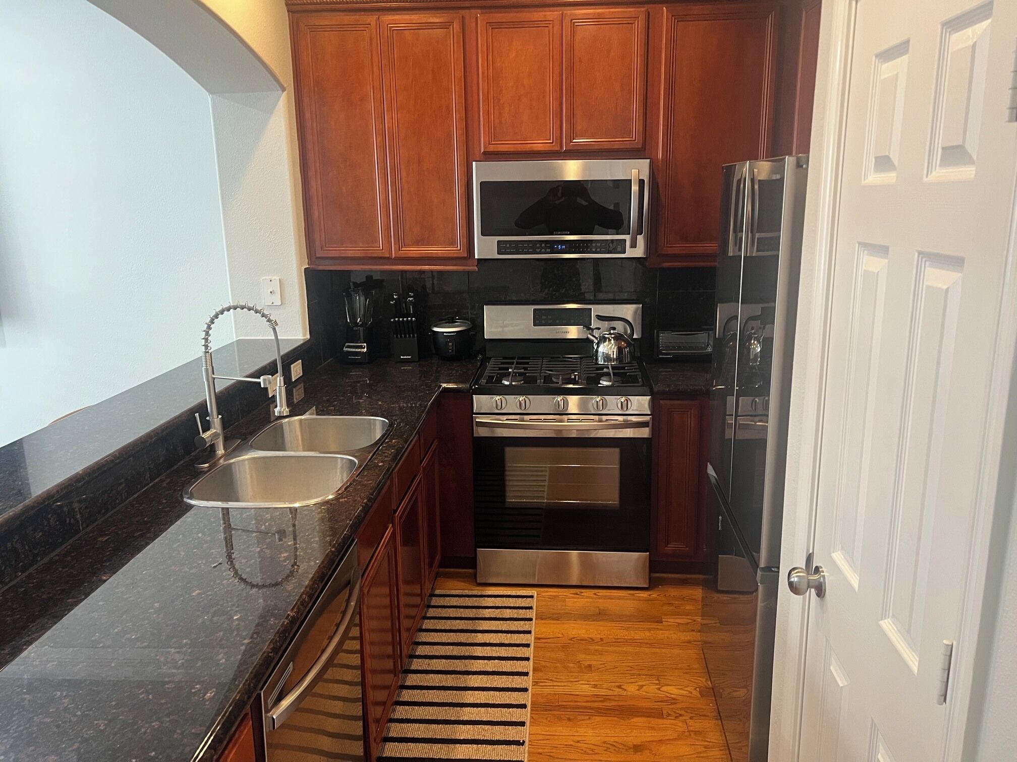 A compact kitchen with wooden cabinets, stainless steel appliances, a double sink, and a small rug.