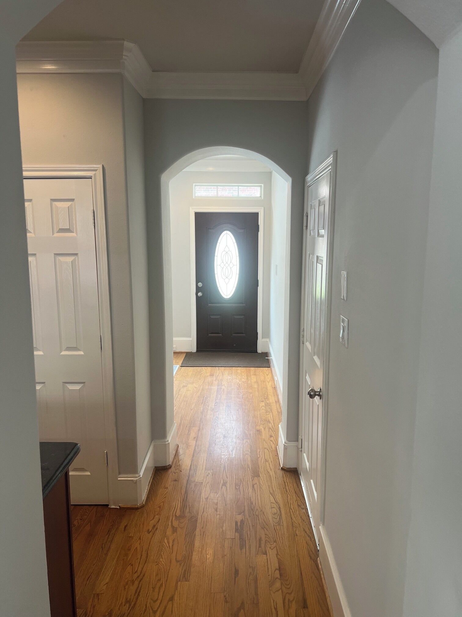 A hallway with wooden flooring, white doors, and a dark-colored door at the end.