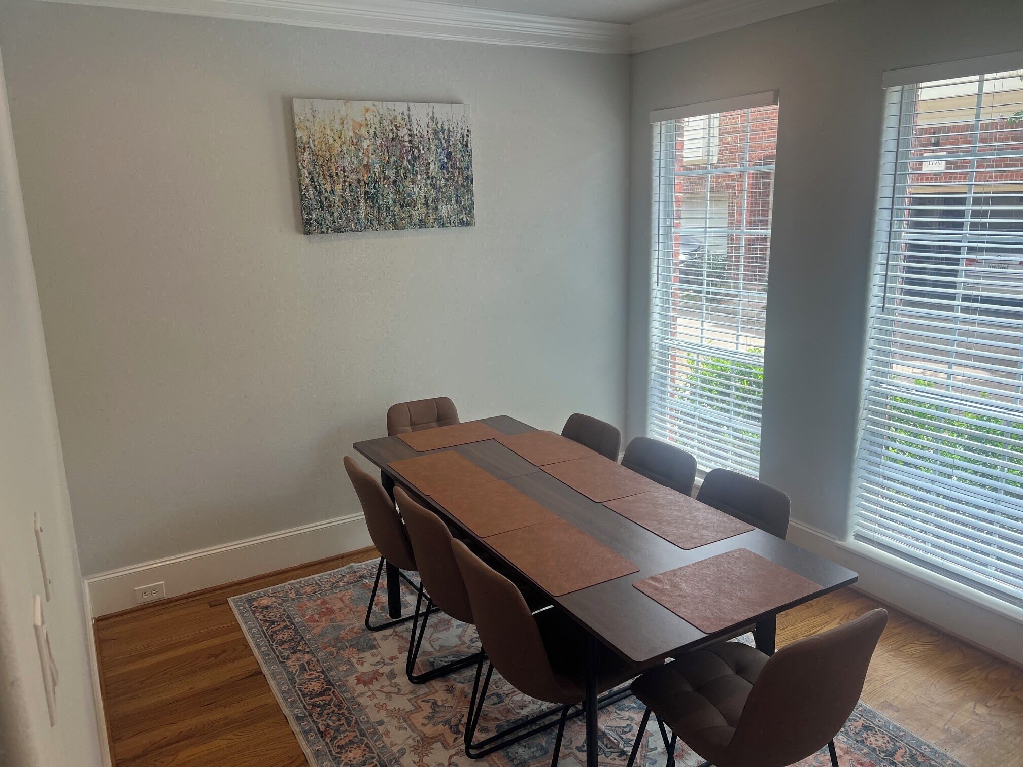 A conference room with a long table, six chairs, a patterned rug, and a large abstract painting on the wall.