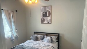 A bedroom with a bed, a ceiling fan, a window with curtains, and a wall-mounted abstract painting. - Beautiful Condo with newly appliances, bedroom sets located at the East Downtown (Houston)