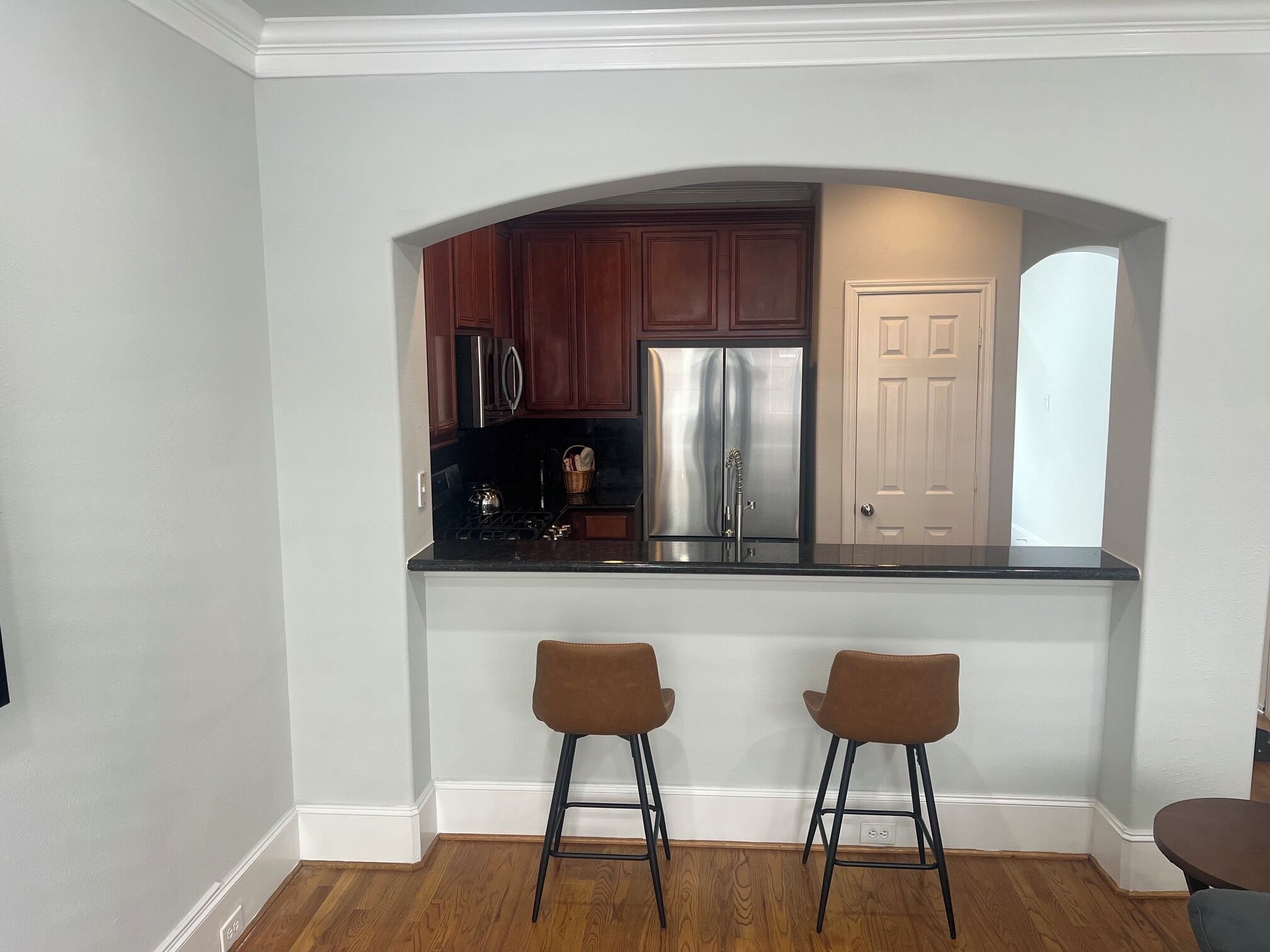 A kitchen with a stainless steel refrigerator, wooden cabinets, and a white door. There are two bar stools and a countertop.