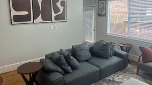 A living room with a grey sofa, a small round table, and a ceiling fan. - Beautiful Condo with newly appliances, bedroom sets located at the East Downtown (Houston)