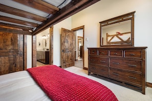 Ein Schlafzimmer mit Bett, Kommode, Spiegel und einer Tür zu einem anderen Raum.