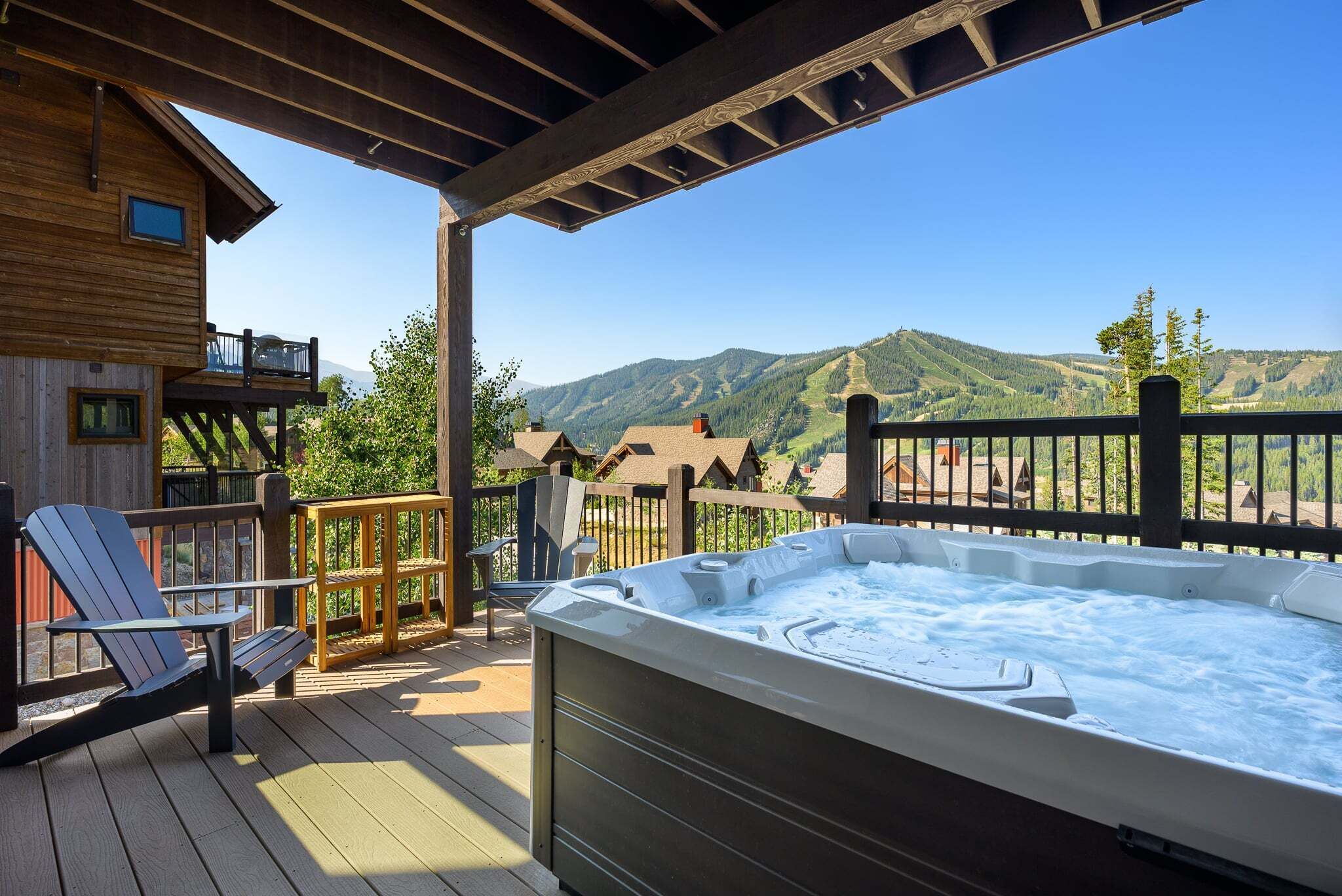 Una terraza de madera con jacuzzi, asientos y vistas a las montañas.