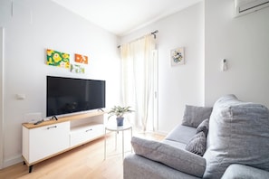 Uma sala de estar moderna com uma televisão de tela plana, um sofá cinza e uma pequena mesa lateral com uma planta.