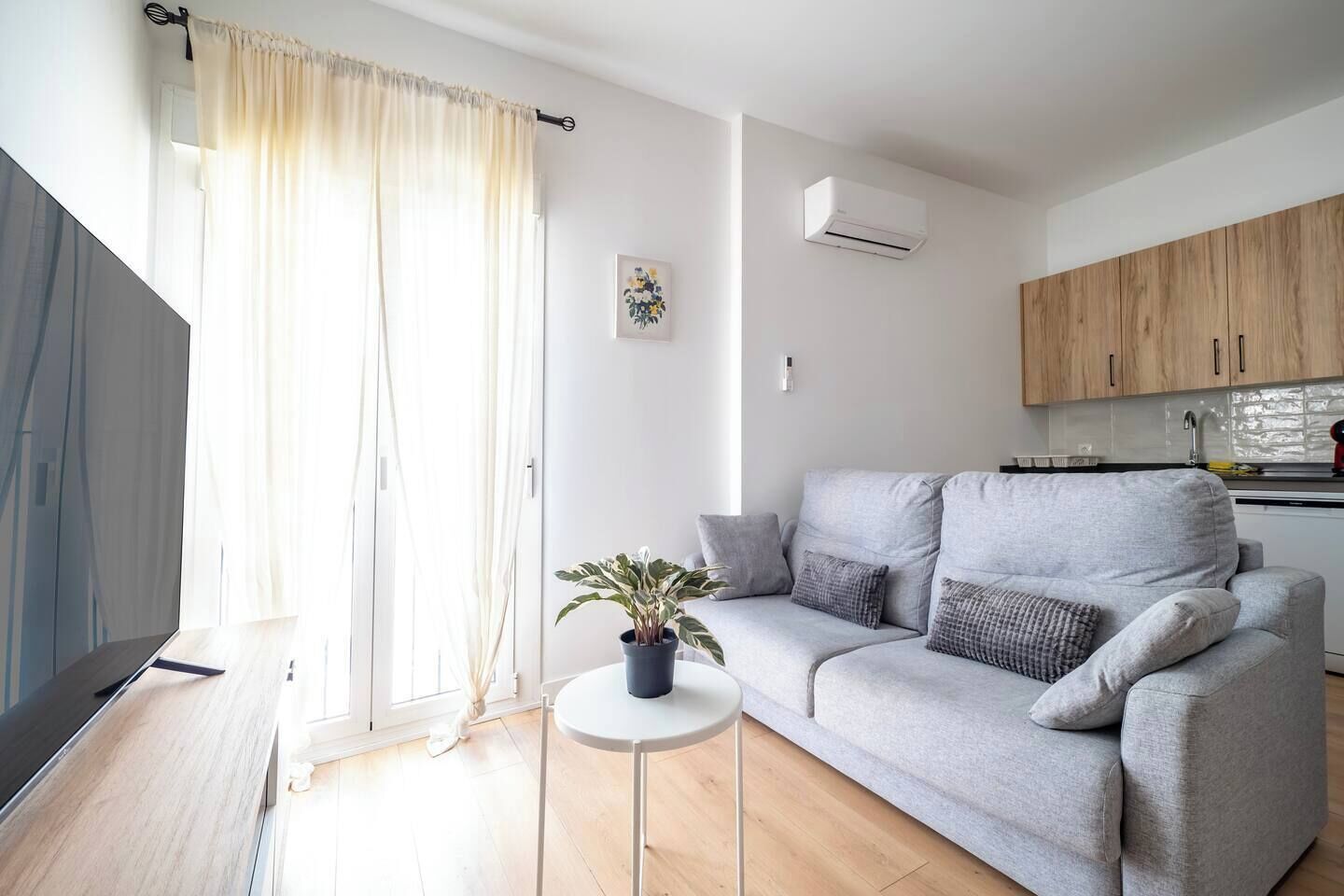 Uma sala de estar moderna com um sofá cinzento, uma mesa redonda pequena com uma planta e uma televisão.