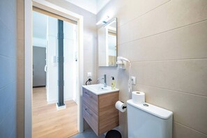 Casa de banho moderna com toucador de madeira, sanita, espelho e secador de cabelo.