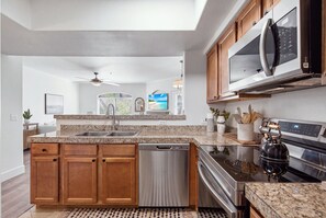 A modern kitchen with granite countertops, stainless steel appliances, wooden cabinets, and a built-in dishwasher. - Signature Scottsdale - 2 bed Condo with Pool View (Scottsdale)