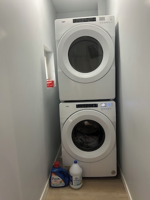 A laundry room with two stacked washing machines and a bottle of laundry detergent. - Waterfront Views! Steps to Caesars & Downtown (Windsor)