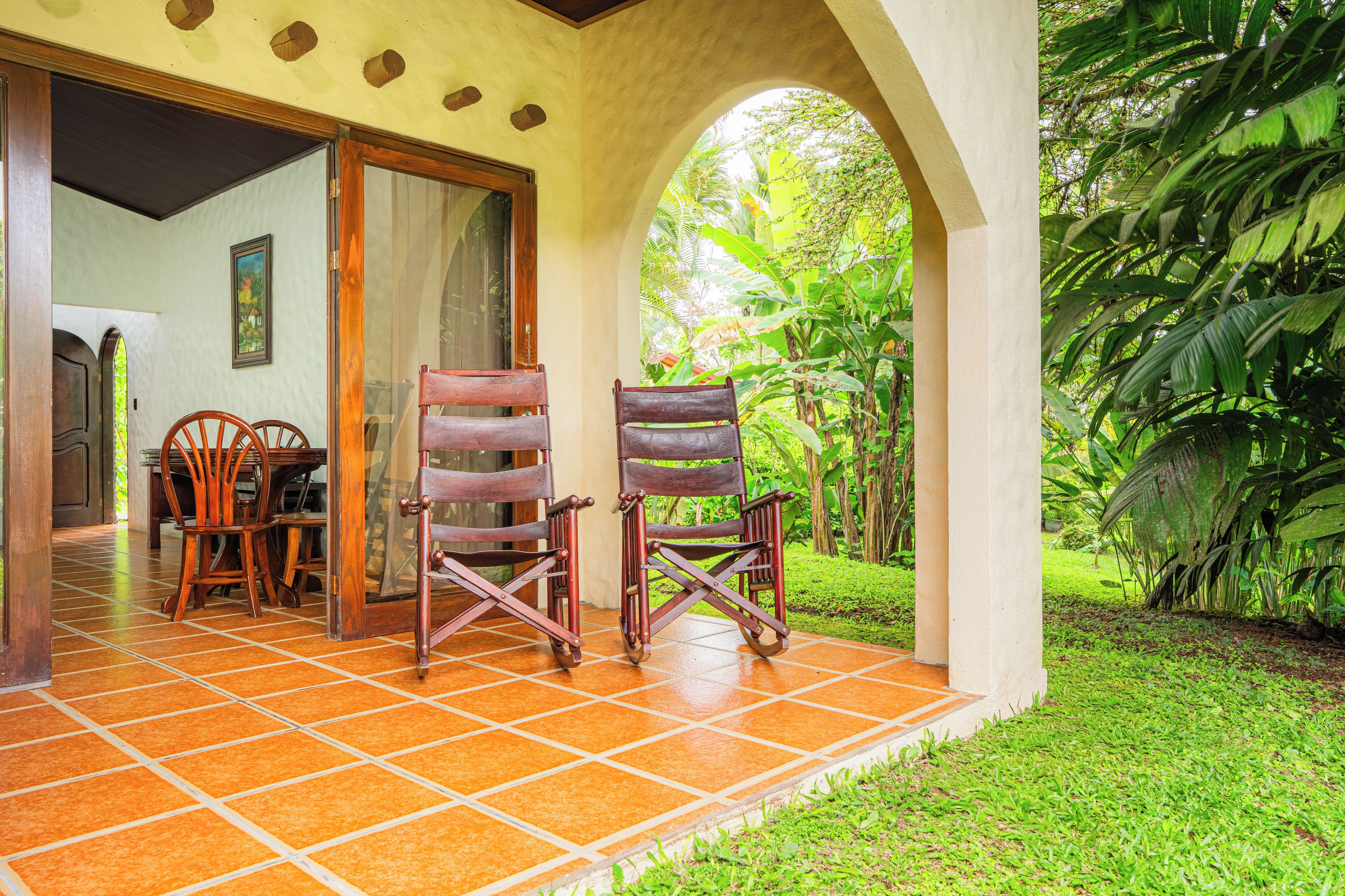 A patio with two wooden chairs, a tiled floor, and a view of lush greenery.