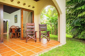 A patio with two wooden chairs, a tiled floor, and a view of lush greenery. - Arenal Rainforest (La Fortuna)